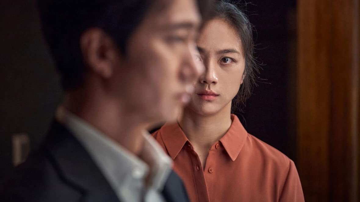 Tang Wei's character stares contemplatively at Park Hae-il. Half of her face is obscured by his out of focus side profile.